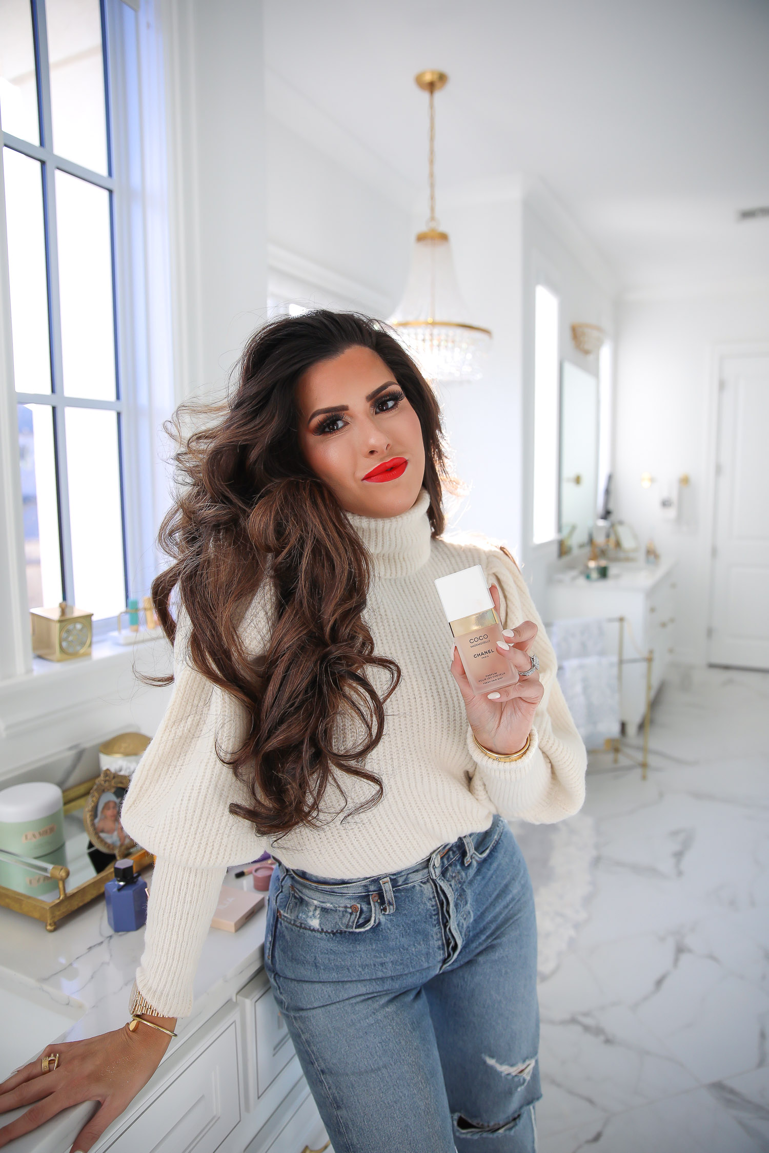 Chanel mademoiselle hair perfume review, Emily Gemma, beauty blogger |Sephora Favorites by popular US beauty blog, The Sweetest Thing: image of a woman wearing a cream turtleneck sweater, distressed denim and standing next to her bathroom vanity while holding Coco Chanel perfume.