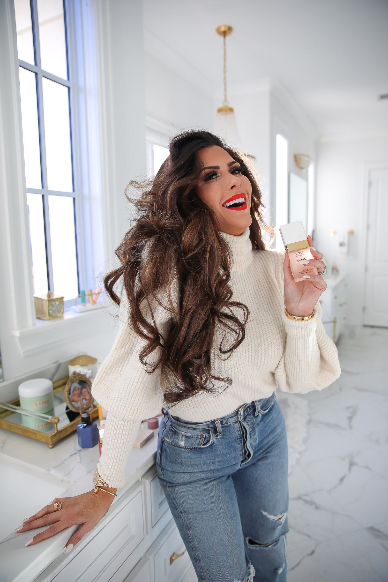 Chanel mademoiselle hair perfume review, Emily Gemma, beauty blogger |Sephora Favorites by popular US beauty blog, The Sweetest Thing: image of a woman wearing a cream turtleneck sweater, distressed denim and standing next to her bathroom vanity while holding Coco Chanel perfume.