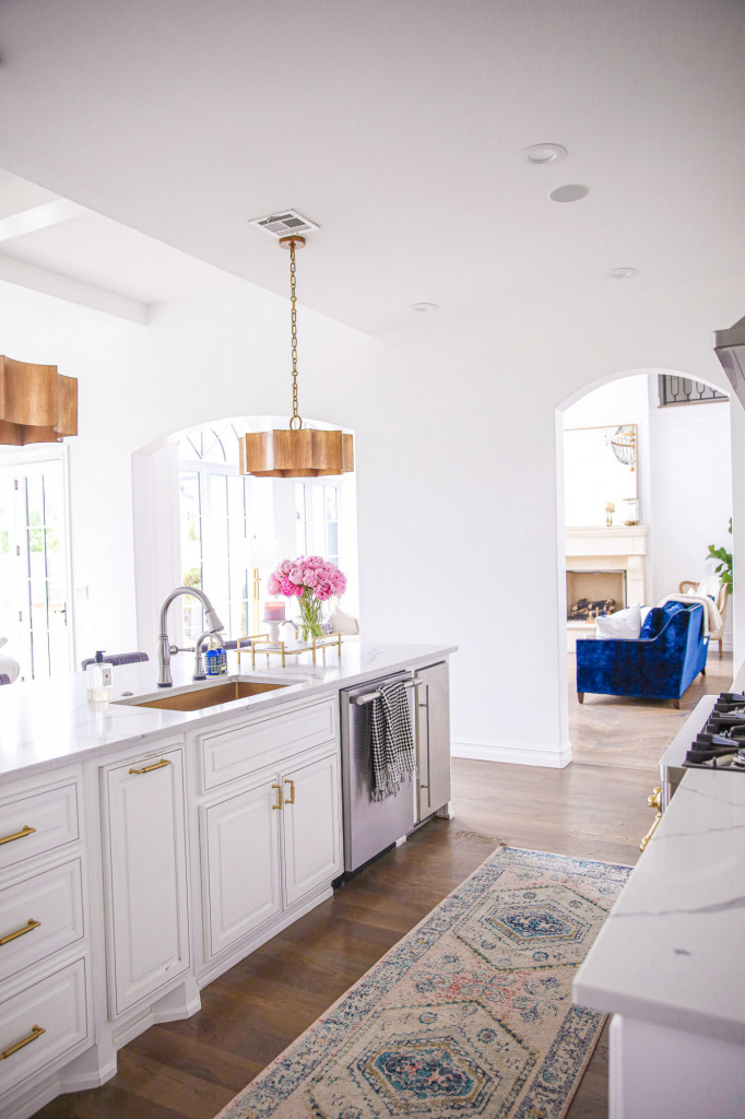 Pinterest white kitchen quartz, ilv majestic stove, Emily Gemma kitchen, gold kitchen sink, Emily Gemma kitchen, grey and gold barstools | Spring Kitchen by popular US life and style blog: image of a kitchen with white cabinets, wood flooring, wooden light pendants, marble counter tops, grey velvet and gold metal bar stools, vase of pink peonies and light pink and blue runner rug.